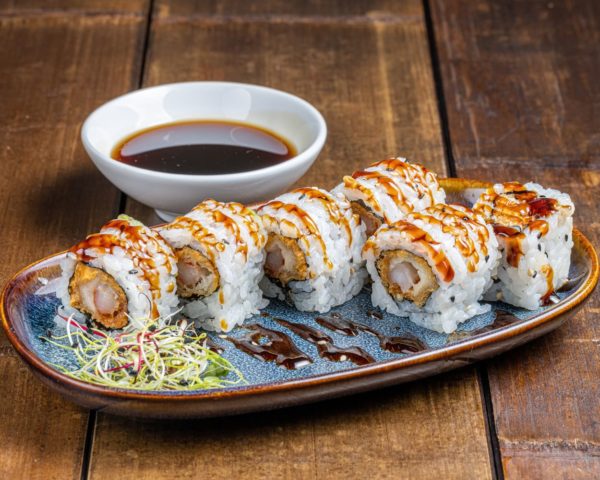 California-roll-crevettes-tempura. California roll de 6 pièces garnies de crevettes tempura croustillantes, nappées d'une sauce cocktail savoureuse, présentées de manière élégante.