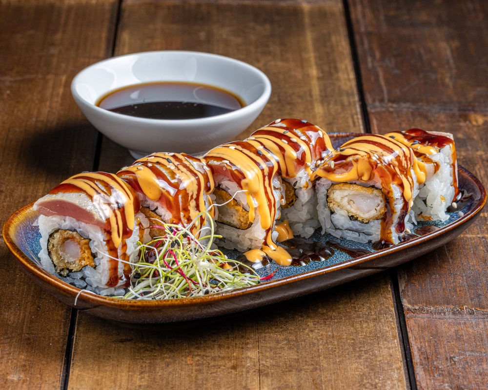 Rouleau Dragon Tuna Tempura avec thon épicé à l'extérieur et un mélange riche de thon, asperge, avocat, masago et sauce épicée à l'intérieur.