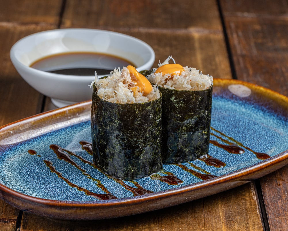 Gunkan garni de chair de crabe tendre mélangée à une mayonnaise onctueuse, entouré d'une bande d'algue nori, sur un lit de riz vinaigré.