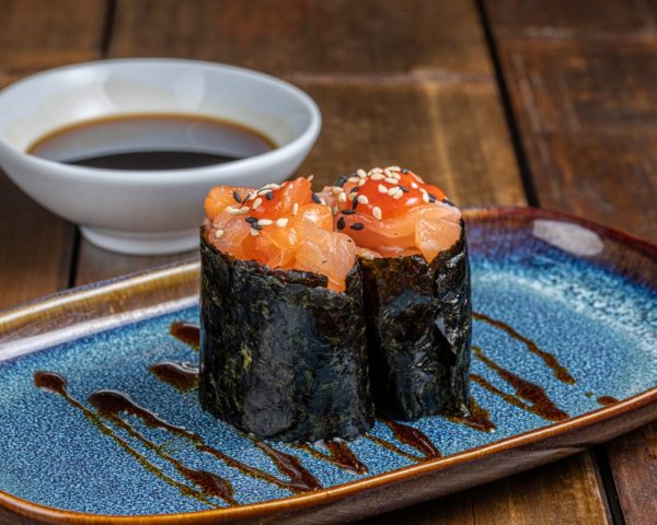 Gunkan délicatement façonné, garni de saumon épicé finement haché, entouré d'une bande d'algue nori, sur un lit de riz vinaigré.