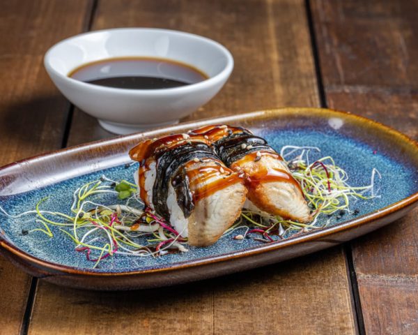 Nigiri-anguille Nigiri méticuleusement préparé, surmonté d'une tranche d'anguille grillée lustrée de sauce, reposant sur un lit de riz vinaigré.