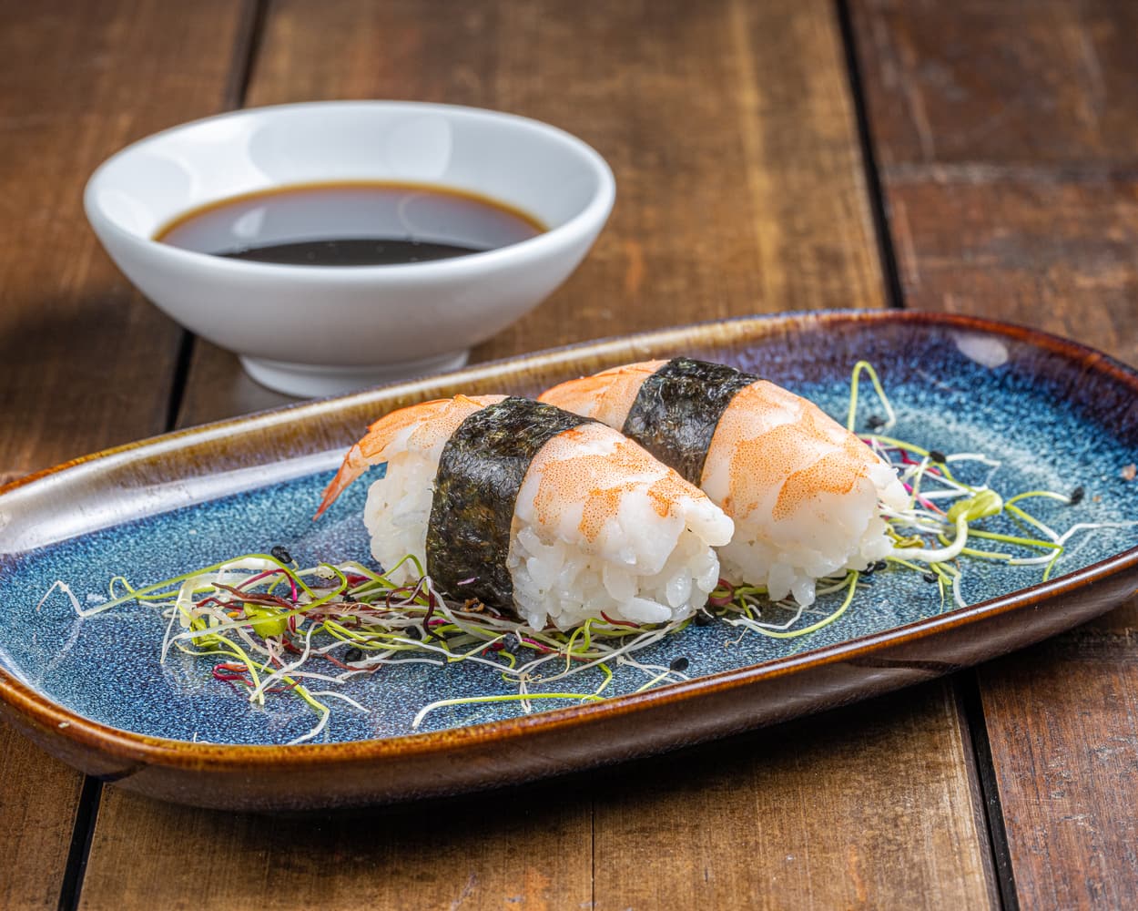 Nigiri soigneusement préparé, surmonté d'une crevette ebi juteuse et brillante, reflétant la saveur délicate de l'océan sur une base de riz vinaigré.