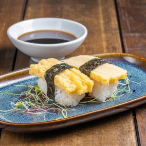 Nigiri délicatement préparé, surmonté d'une tranche d'omelette japonaise tamago moelleuse et dorée, reposant sur un lit de riz vinaigré.