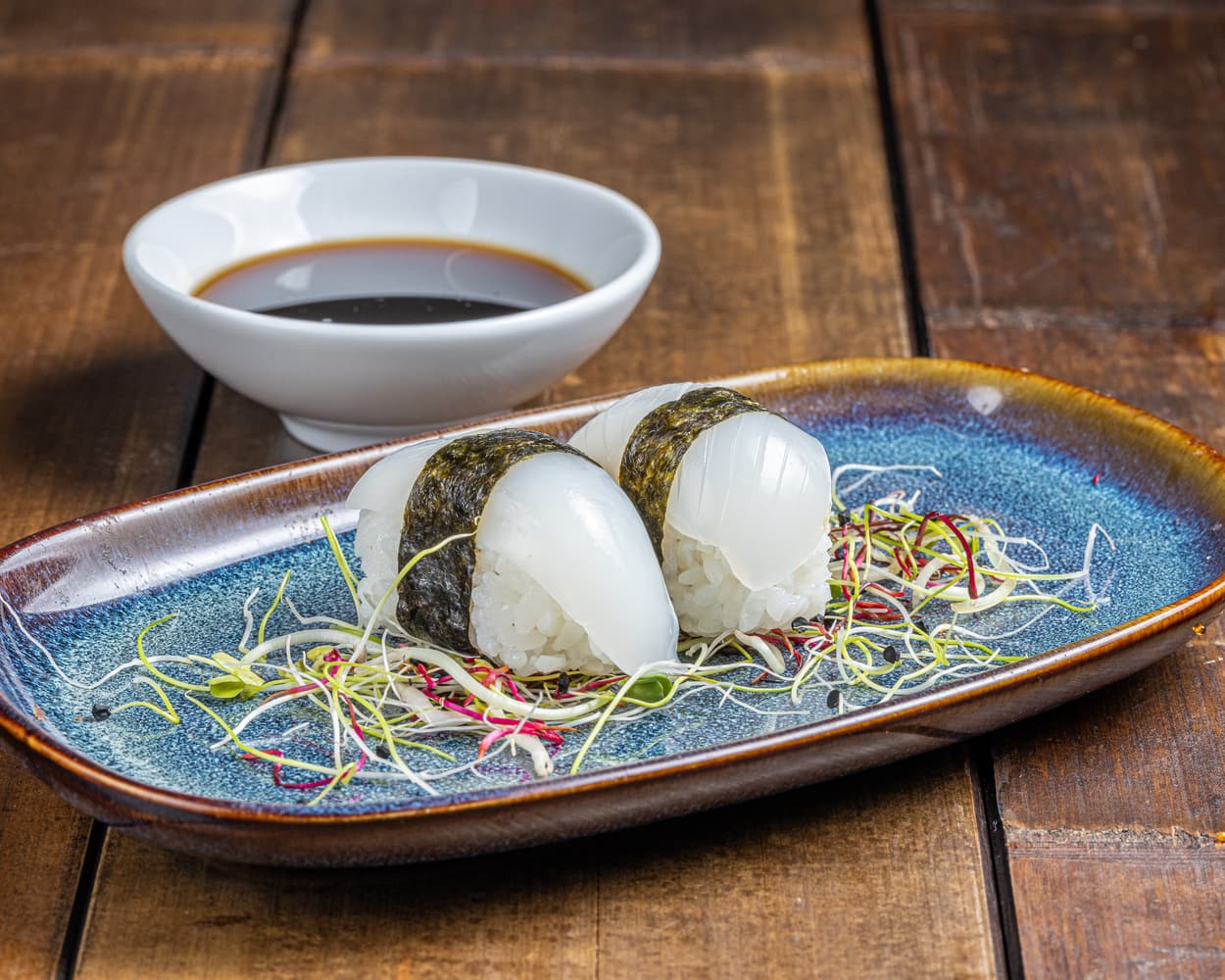 Nigiri soigneusement façonné, couronné d'une tranche de seiche fraîche et translucide, reposant sur un lit de riz vinaigré.