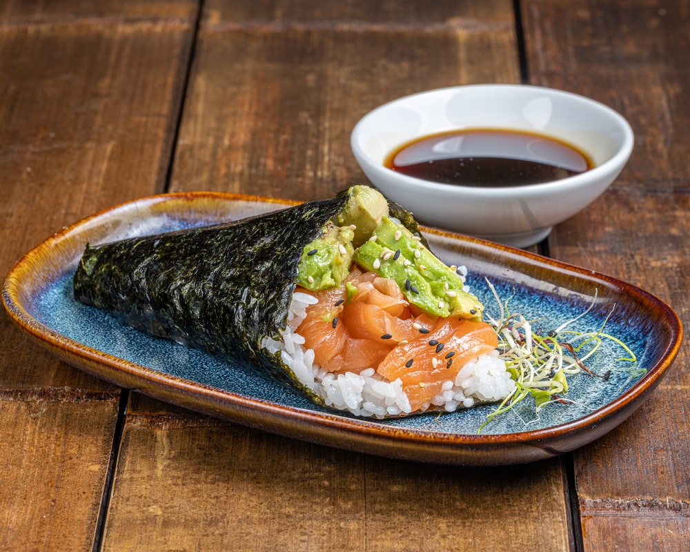 Temaki en forme de cône garni de saumon frais, crème cheese onctueuse et tranches d'avocat, enveloppé dans une feuille de nori.