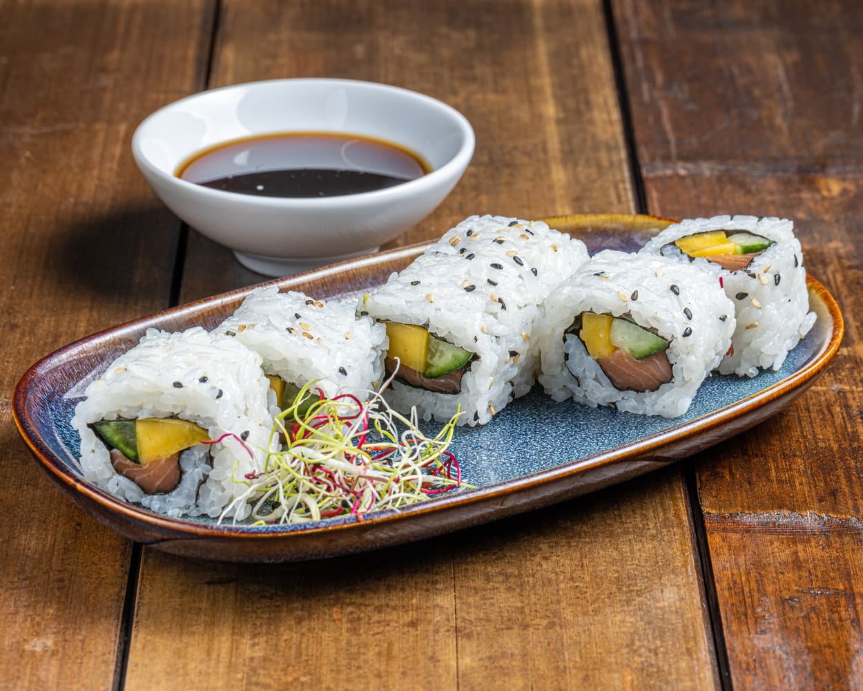 California roll garni de saumon frais, tranches de mangue sucrée et concombre croquant, présenté de manière élégante pour une combinaison tropicale et rafraîchissante.